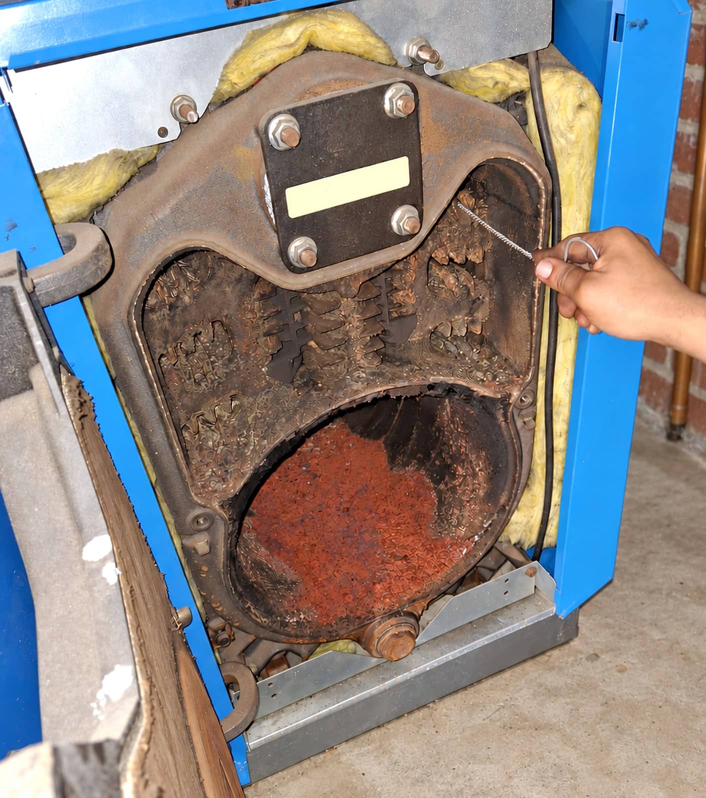 Chaudière au mazout Buderus ouverte pendant un entretien, foyer encrassé et rouillé, main tenant une brosse de nettoyage
