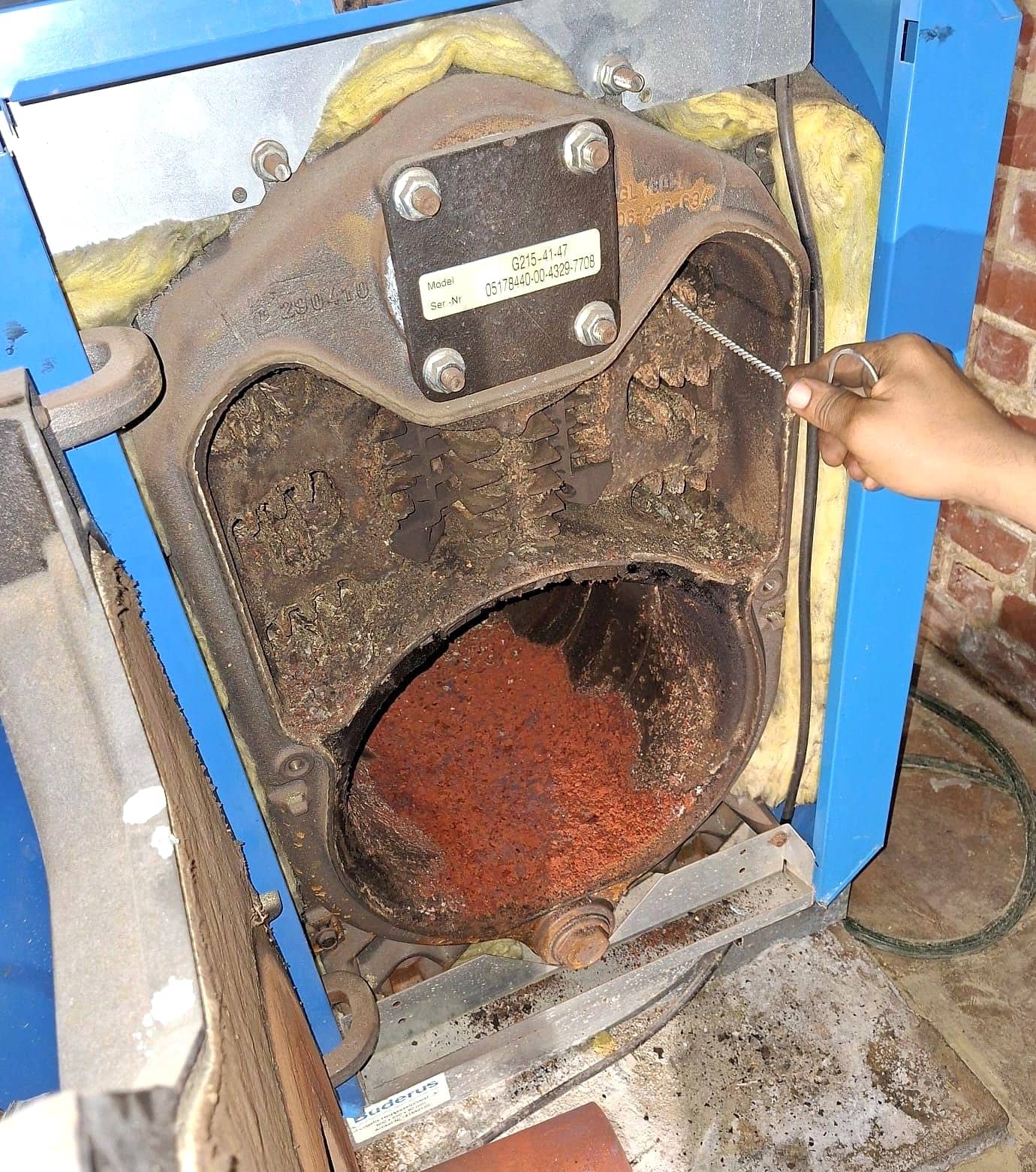 Chaudière au mazout Buderus ouverte pendant un entretien, foyer encrassé et rouillé, main tenant une brosse de nettoyage