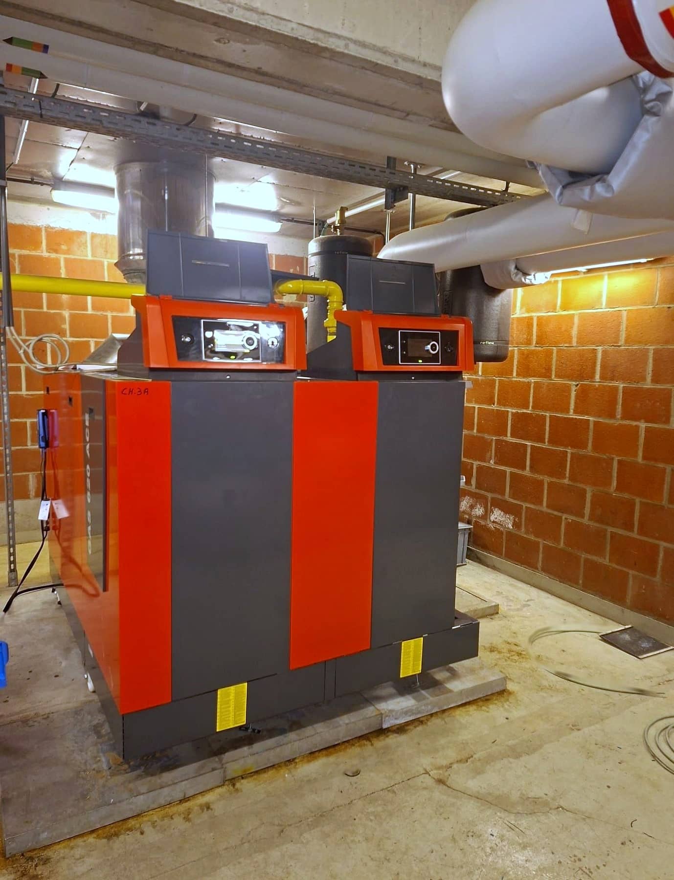 Chaufferie collective avec deux chaudières Remeha Gas 620 Ace rouge et anthracite, conduite de gaz jaune et vases d’expansion