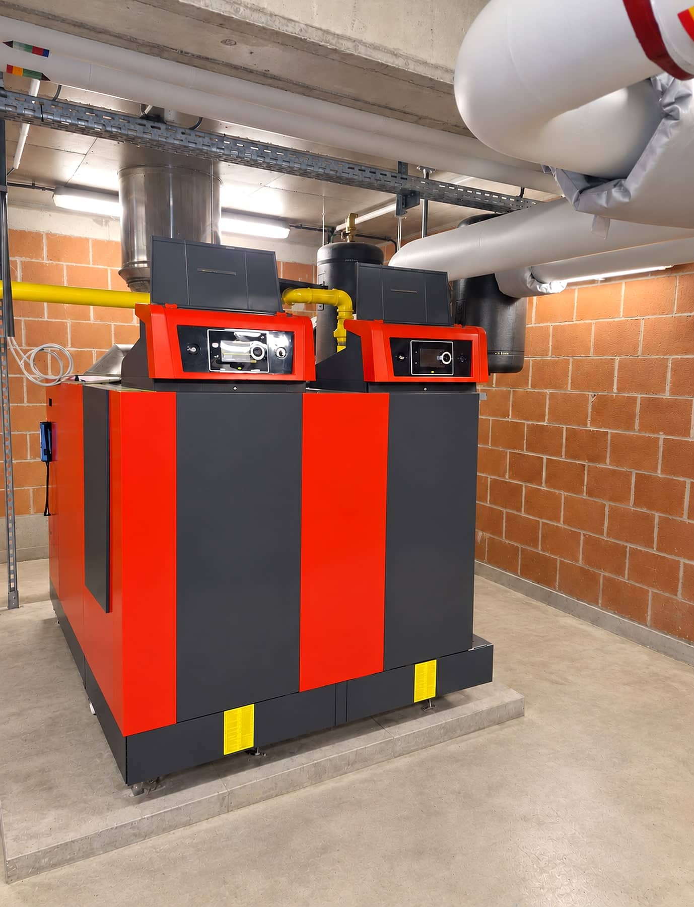 Chaufferie collective avec deux chaudières Remeha Gas 620 Ace rouge et anthracite, conduite de gaz jaune et vases d’expansion