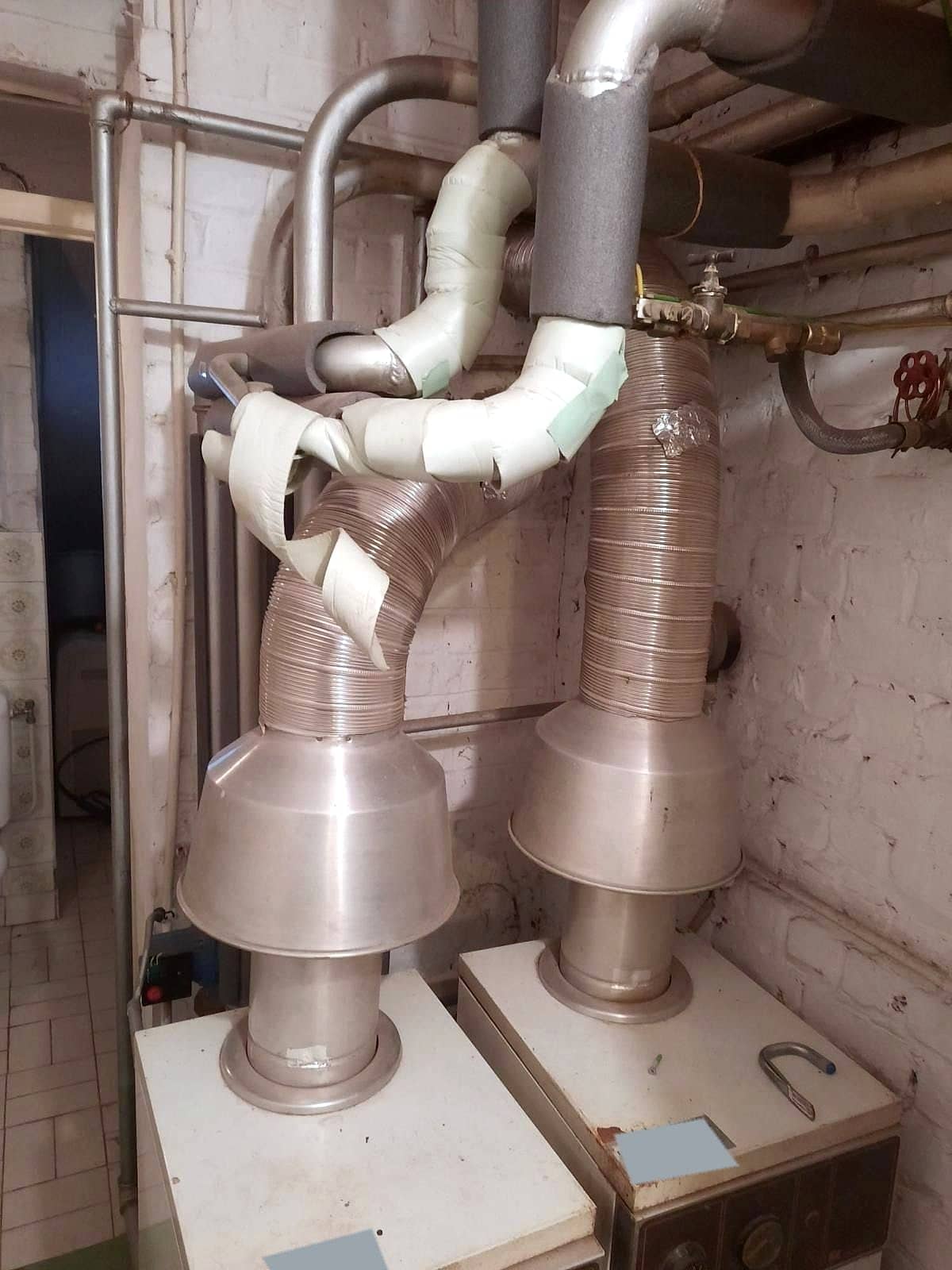 Deux anciennes chaudières au sol dans une cave, conduits d’évacuation flexibles en aluminium et isolants tenus au ruban adhésif